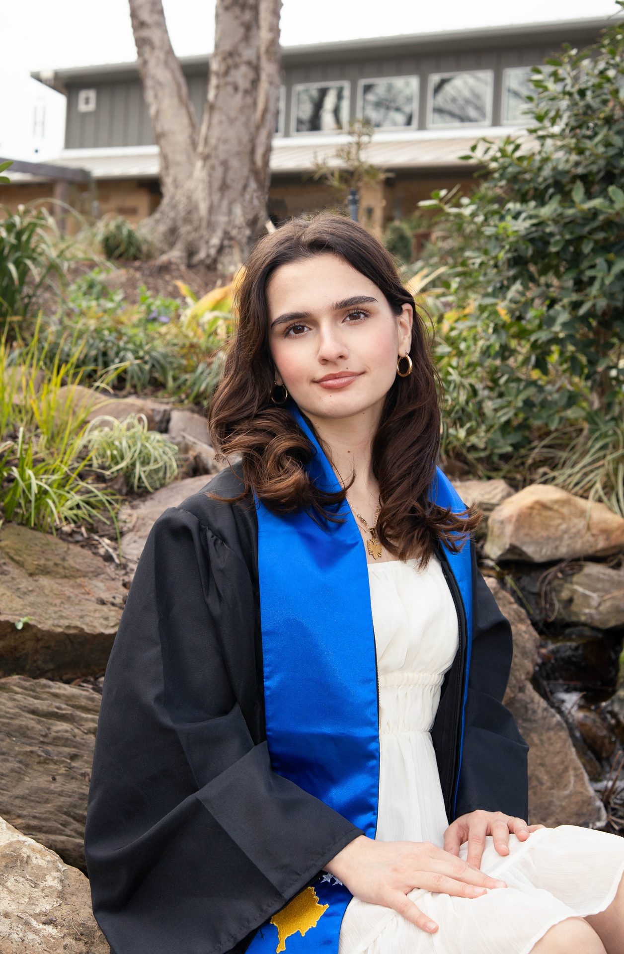 Graduate in cap and gown at outdoor garden arch, DFW graduation photography by Rayala Photo